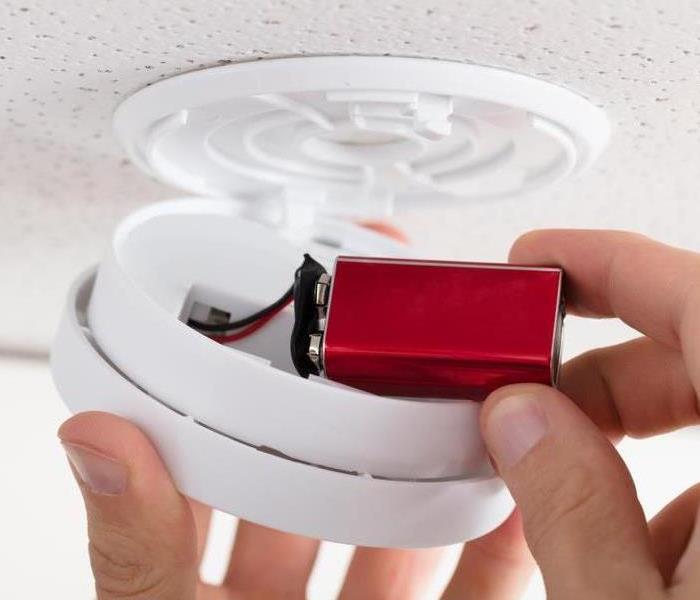 A person putting a battery in a fire alarm.